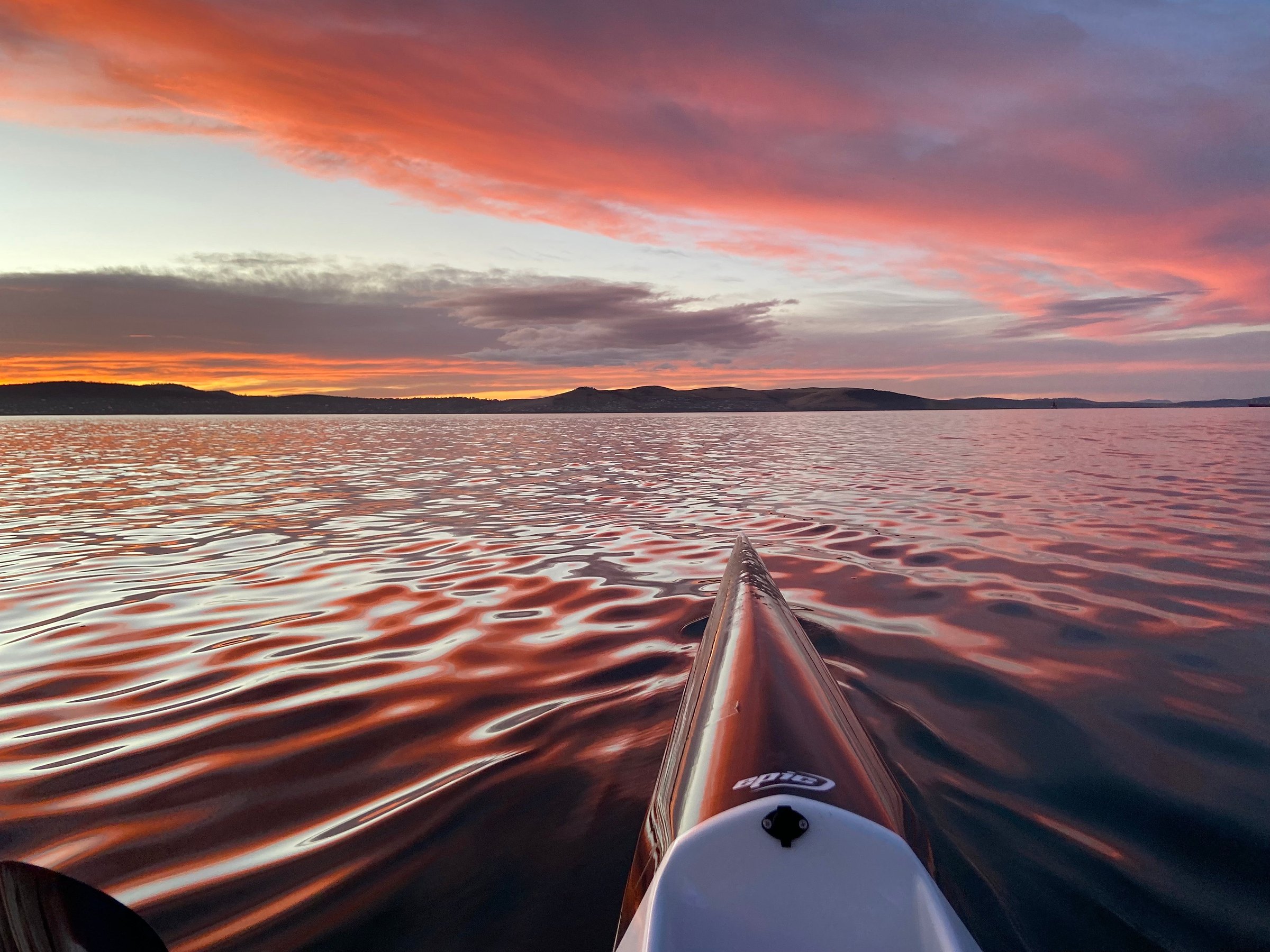 The bow of an Epic surfski on glassy water at sunrise